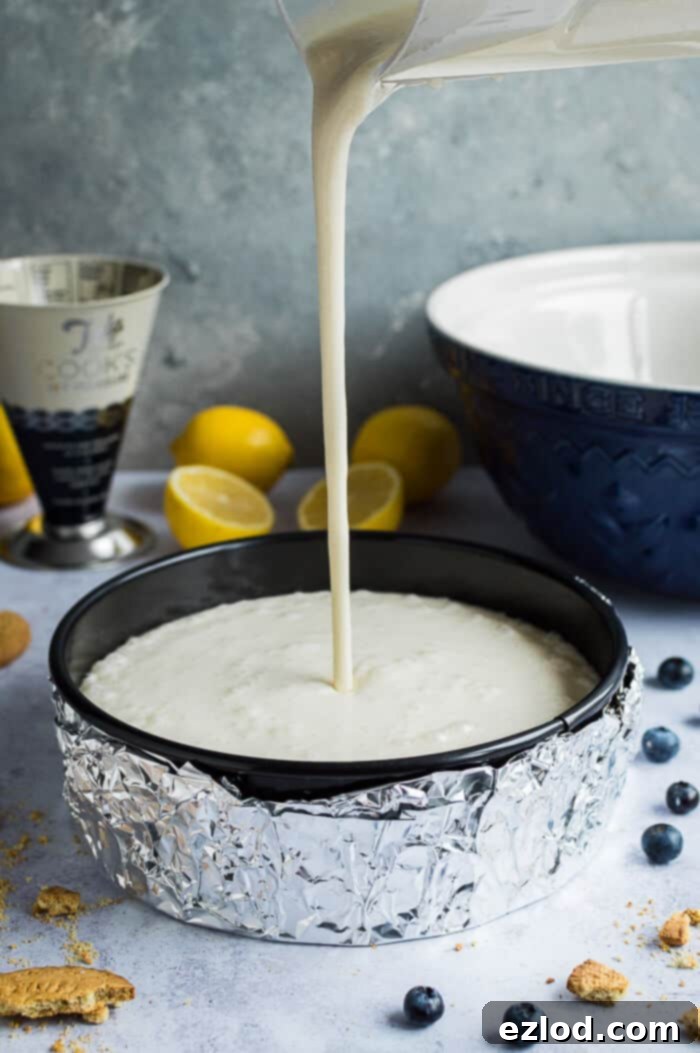 Pouring the creamy vegan lemon cheesecake filling into a Tala springform cake tin over the baked biscuit base.