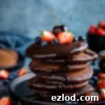 Decadent Vegan Chocolate Fluff Pancakes with Sauce 5 A stack of vegan chocolate pancakes on a black plate topped with chocolate sauce and fresh berries.