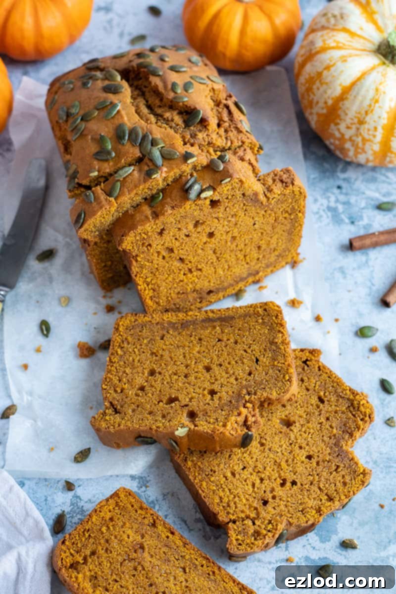 Cooling and Slicing Your Perfect Vegan Pumpkin Loaf A freshly baked and sliced loaf of vegan pumpkin bread elegantly arranged on a blue background, complemented by small decorative pumpkins.