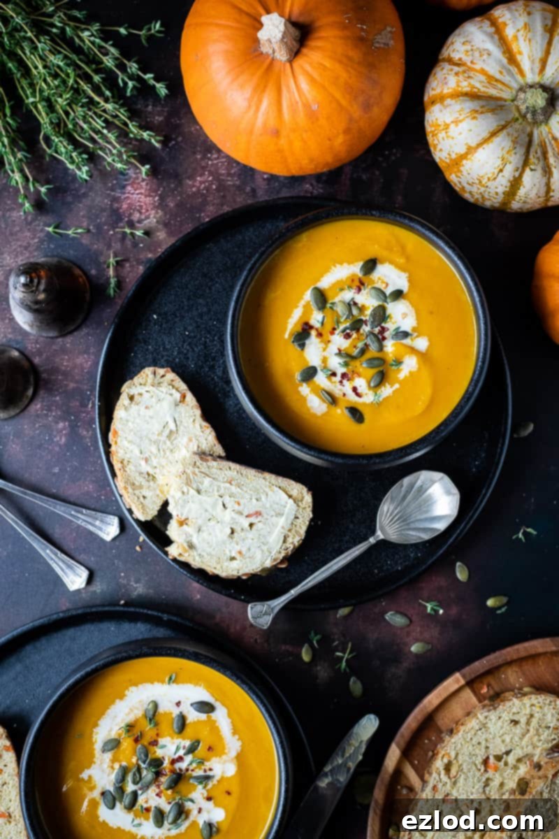 Vegan Spiced Carrot and Pumpkin Soup Two black bowls filled with vegan spiced carrot and pumpkin soup, garnished with fresh thyme sprigs, presented on dark plates with mini pumpkins and fresh bread in the background.