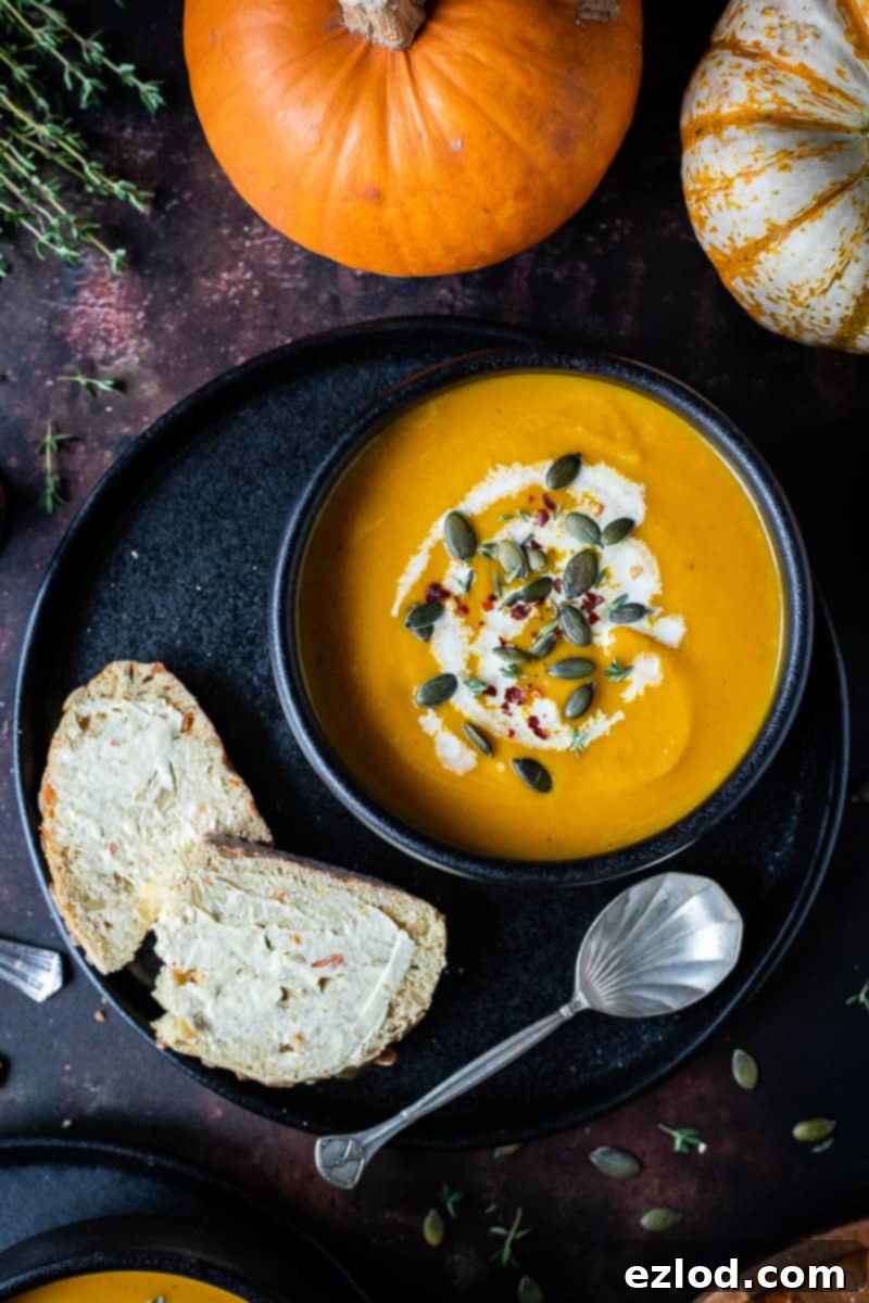 Vegan Spiced Carrot and Pumpkin Soup Close-up of a black bowl filled with creamy vegan spiced carrot and pumpkin soup, topped with a swirl of plant-based cream, pumpkin seeds, and a few chili flakes.