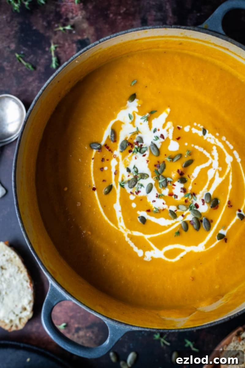Vegan Spiced Carrot and Pumpkin Soup Close-up of a cast iron pan filled with creamy vegan spiced carrot and pumpkin soup, garnished with plant-based cream, pumpkin seeds, and chili flakes.
