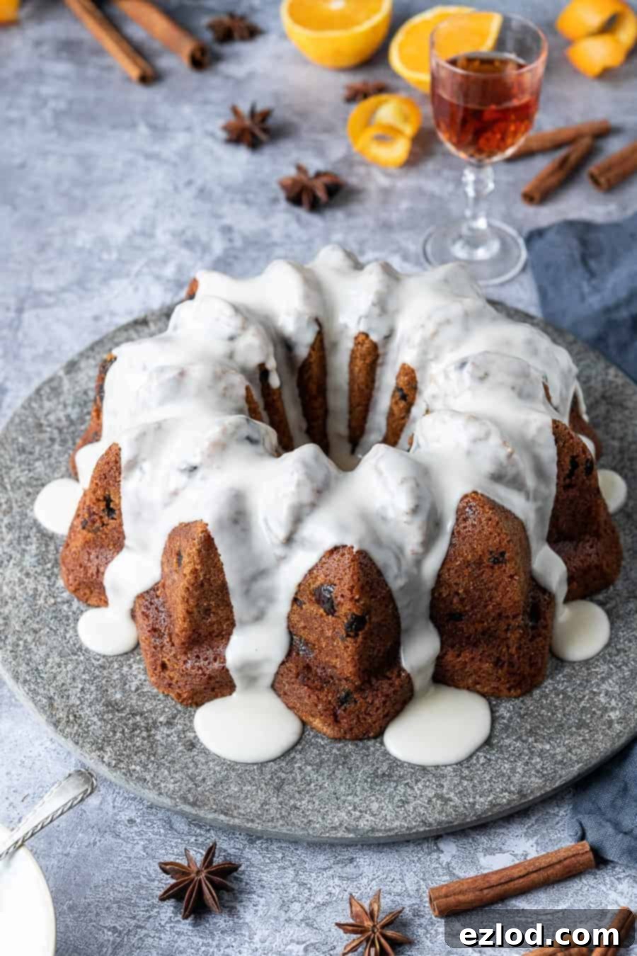 Vegan mincemeat cake - this Christmassy vegan bundt cake is perfect for using up mincemeat (of the fruit variety!) or is a great festive alternative to a traditional Christmas cake. #bundtcake #vegancake #veganbaking #christmascake #christmas #festive #mincemeat vegan mincemeat cake on a grey stone plate with oranges, spices and a glass of whisky in the background.