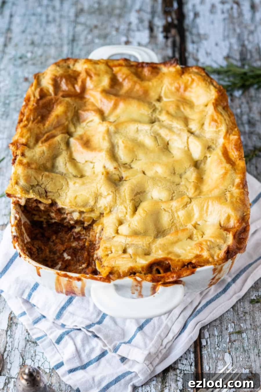 Classic vegan lasagne - this vegan lasagna is seriously good! A rich mushroom ragu is layered up with a creamy dairy-free bechamel sauce and sheets of pasta. It is hearty, filling, totally delicious and healthy too! #lasagna #veganmeals #veganlasagna #plantbased #dairyfree #meatfree classic vegan lasagne with a slice removed in a white dish on a rustic wooden background.