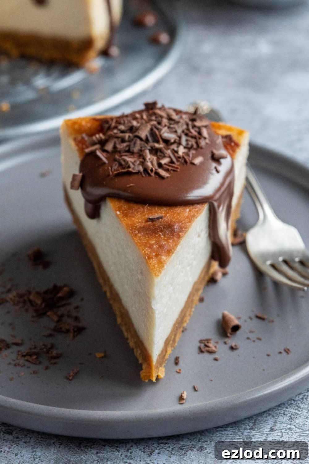 A perfect slice of Vegan Baileys Cheesecake, showing its creamy texture and luscious ganache. Detailed close-up of a single slice of vegan Baileys cheesecake, beautifully topped with velvety chocolate ganache, served on a sophisticated grey plate.