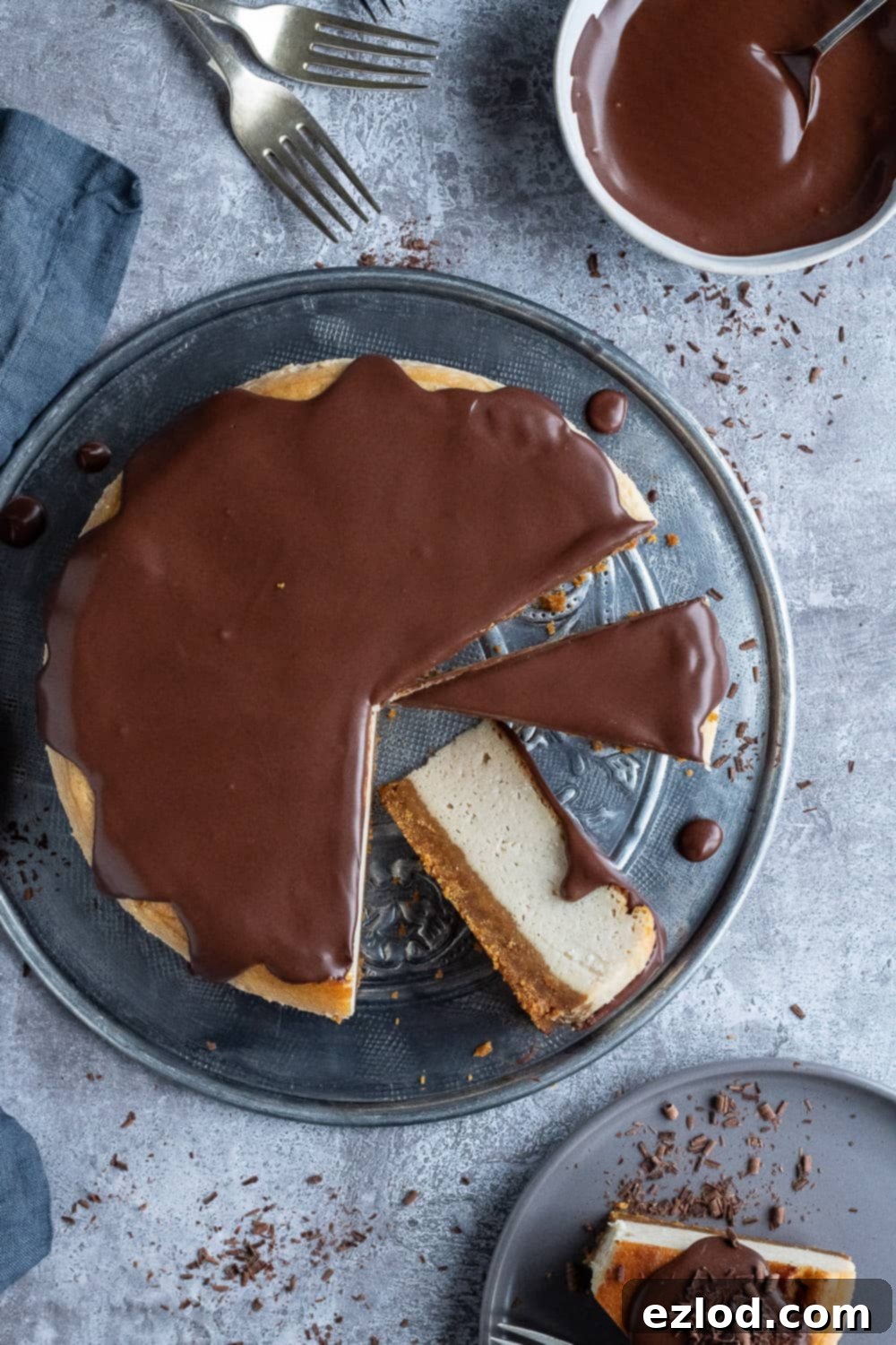 Serving a delightful Vegan Baileys Cheesecake: a top-down view of slices on a platter, showcasing its perfect texture and tempting ganache. A beautiful top-down perspective of a pre-sliced vegan Baileys cheesecake, elegantly presented on a metal plate. A single slice is carefully positioned on a separate grey serving plate, alongside a small bowl of luxurious chocolate ganache.