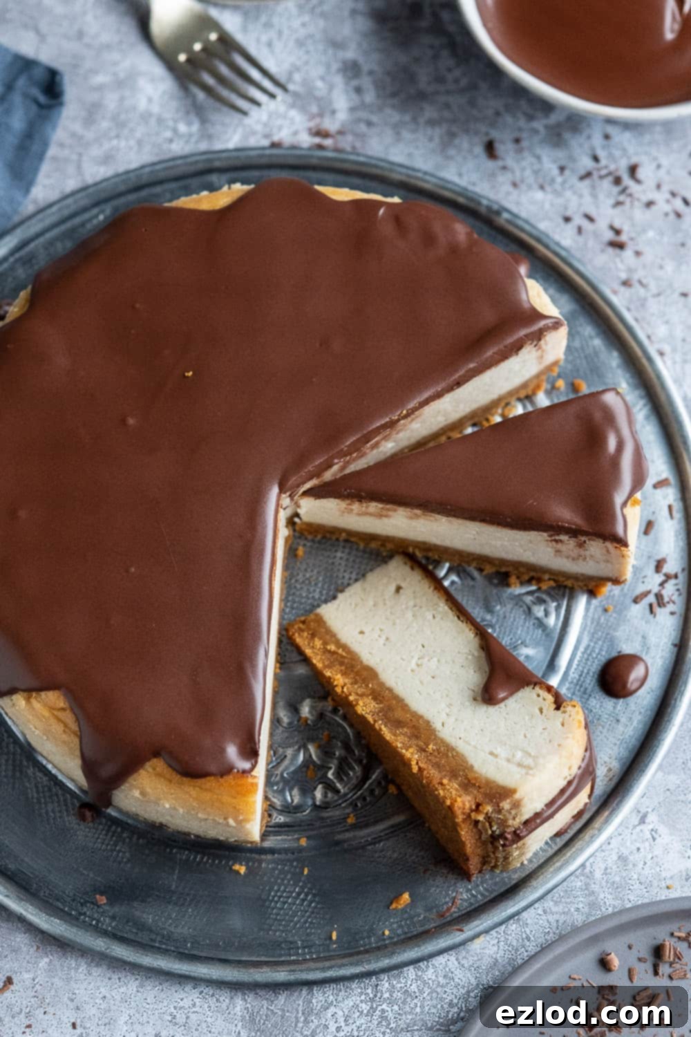 Finished Vegan Baileys Cheesecake with Baileys Ganache, perfect for elegant serving and sharing. A beautifully presented vegan Baileys cheesecake topped with a generous amount of Baileys ganache, sitting on a metal platter with two elegant slices cut and one placed artfully on its side.