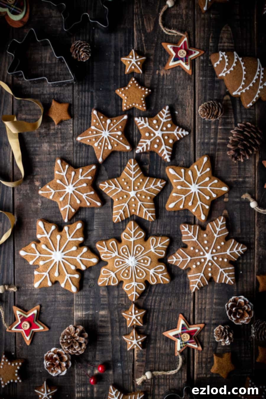 Beautifully decorated vegan gingerbread snowflake cookies arranged in a festive Christmas tree shape, perfect for holiday gatherings or gifts. #veganbaking #vegangingerbread #gingerbread #eggless #dairyfree #Christmas Decorated vegan gingerbread snowflake cookies arranged on a table with pine cones and festive decorations.