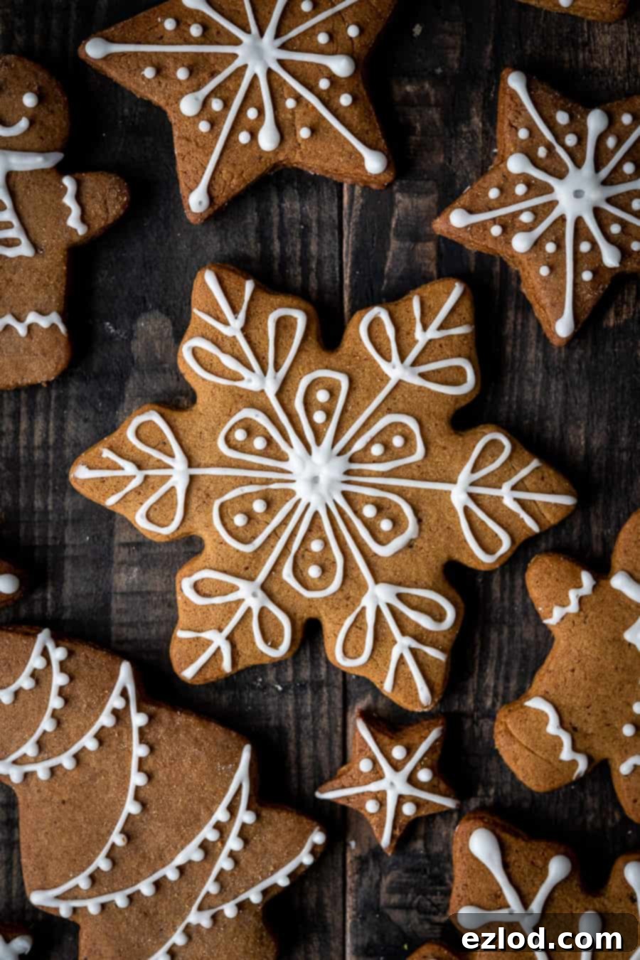 A close-up of a vegan gingerbread snowflake cookie, beautifully decorated with white royal icing, perfect for a festive treat. #veganbaking #vegangingerbread #gingerbread #eggless #dairyfree #Christmas Close-up of a perfectly iced vegan gingerbread snowflake cookie on a dark wood background.