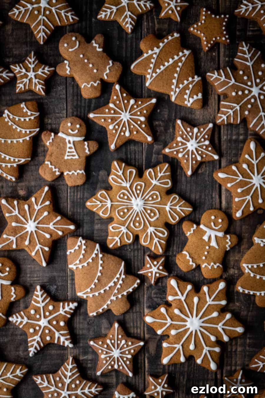 Vegan gingerbread cookies – perfect for holiday decorating or as edible gifts. This easy recipe makes soft or crunchy gingerbread men, snowflakes, or any festive shapes you desire. #veganbaking #vegangingerbread #gingerbread #eggless #dairyfree #Christmas Close-up of freshly iced vegan gingerbread cookies on a rustic dark wood background.