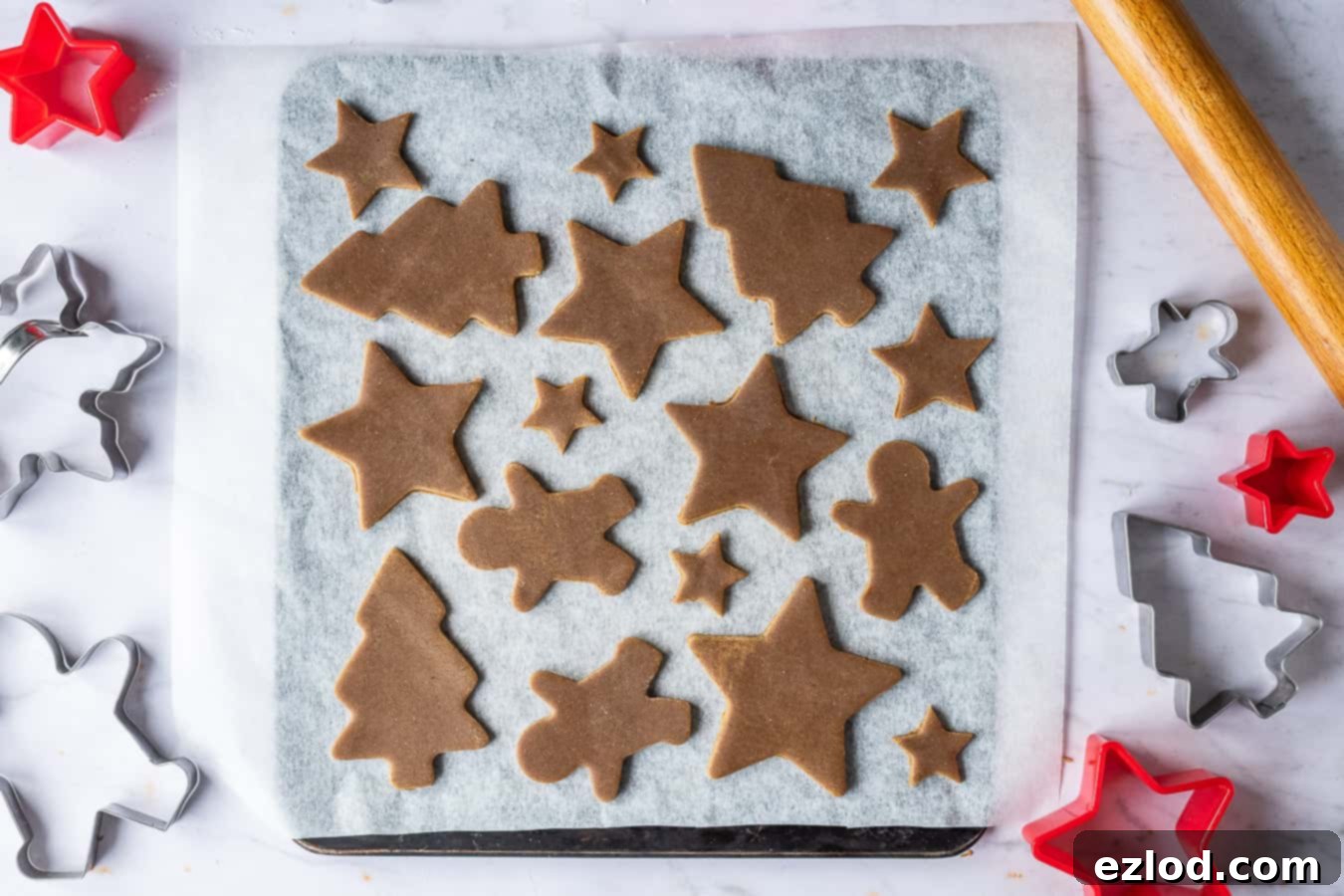 Festive Vegan Gingerbread Cookies 6 Various shapes of vegan gingerbread cookies freshly cut and arranged on a baking sheet lined with parchment.
