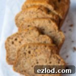 Spiced Vegan Carrot Banana Loaf 4 A loaf of vegan carrot banana bread cut into slices on a sheet of white baking parchment, showing a rich, moist texture.