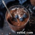 Divine Vegan Chocolate Mousse 5 A glass of mousse on a dark background with a blue cloth and a scattering of chocolate shavings.
