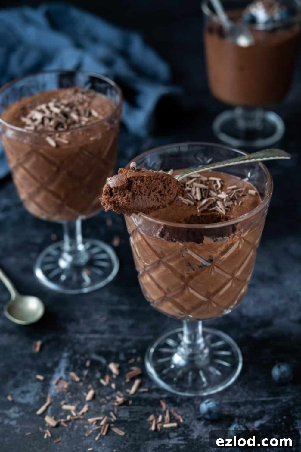 Aquafaba Chocolate Mousse - Easy Eggless Dessert Three glasses of vegan chocolate mousse on a dark background, one glass with a spoonful of mousse balanced on the rim.