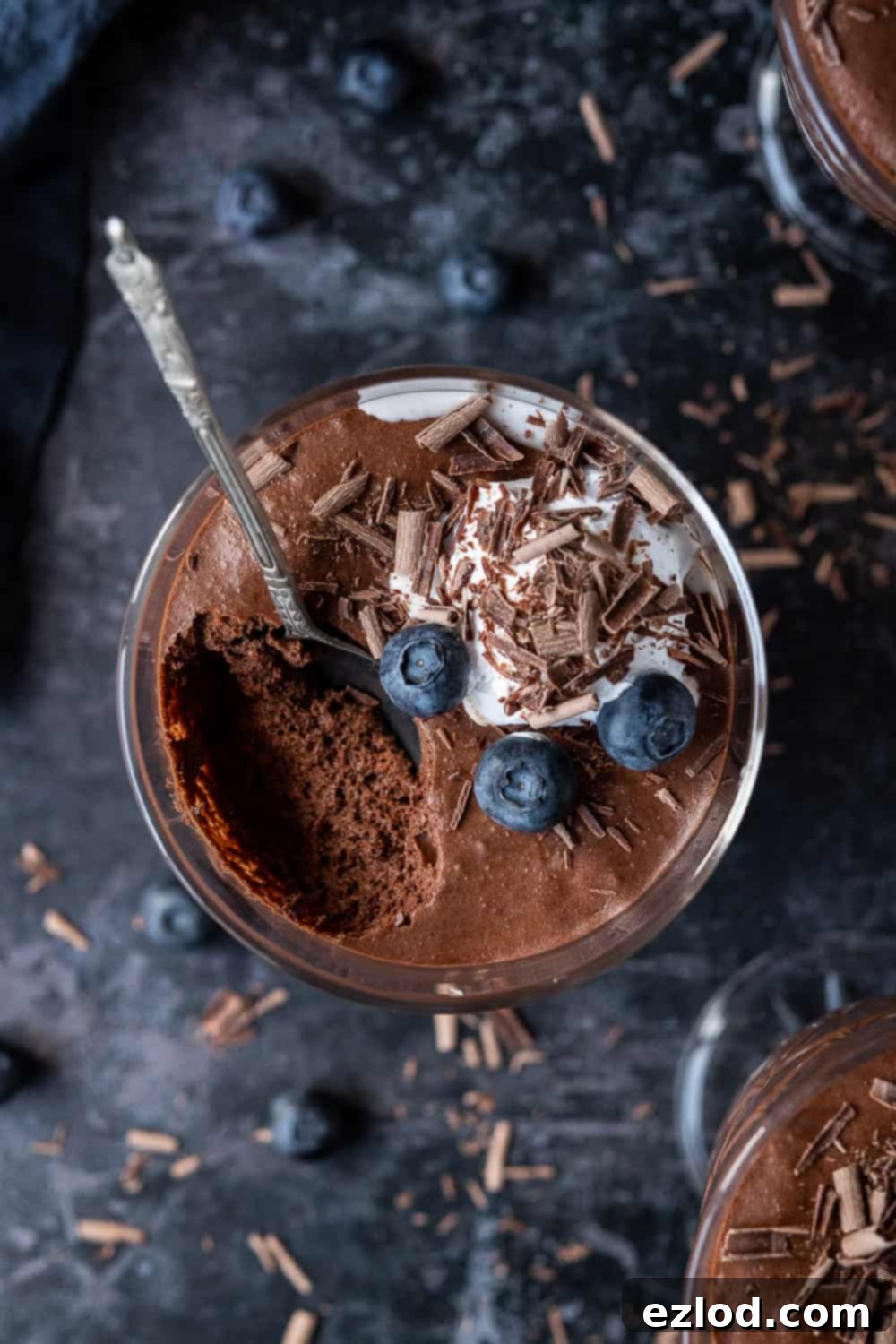 Rich Vegan Chocolate Mousse with Aquafaba Close up of a glass of vegan chocolate mousse with whipped cream, blueberries and chocolate shavings with a spoonful removed.