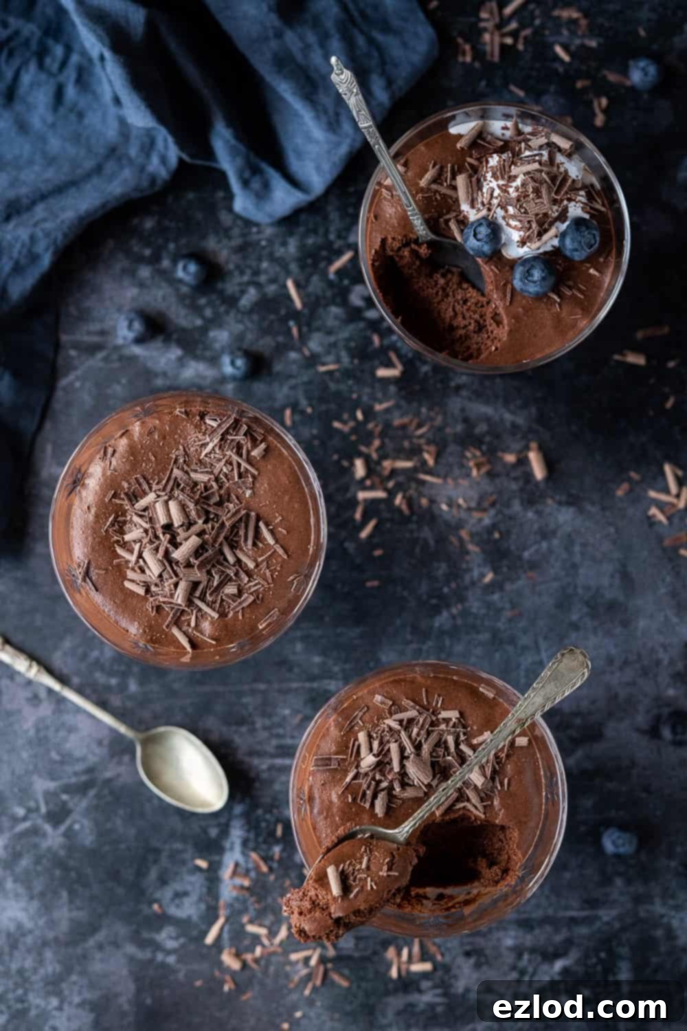 Vegan Chocolate Mousse in Elegant Glasses Top down shot of three glasses of chocolate mousse on a dark background with a blue cloth.