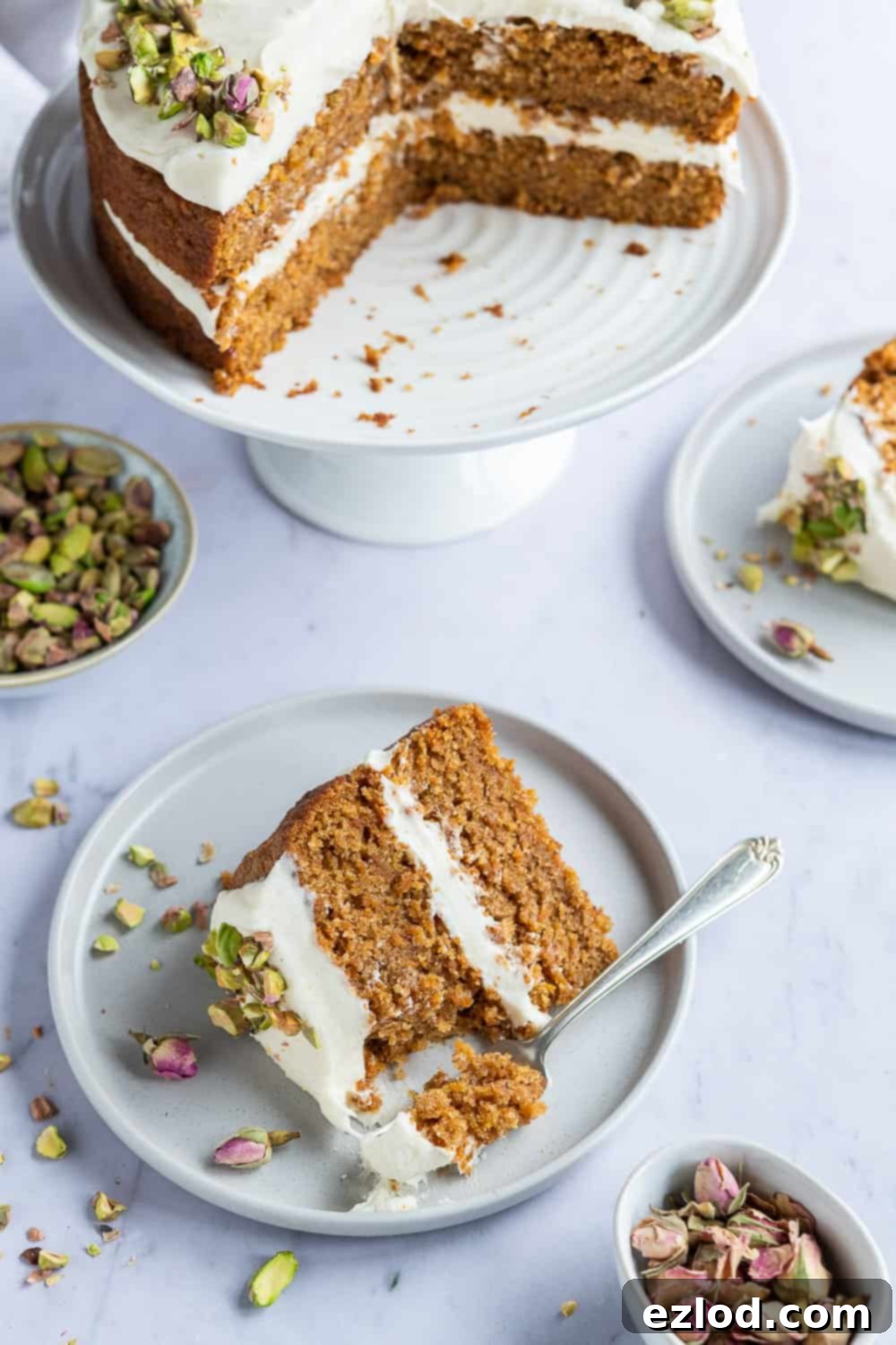 Vegan Carrot Cake Servings Two slices of vegan carrot cake on individual grey plates, displayed alongside the remaining full cake on a white cake stand.