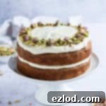 Spiced Vegan Carrot Cake with Tangy Cream Cheese 6 Vegan carrot cake with cream cheese frosting, pistachios and rosebuds on a white cake stand on a marble surface.