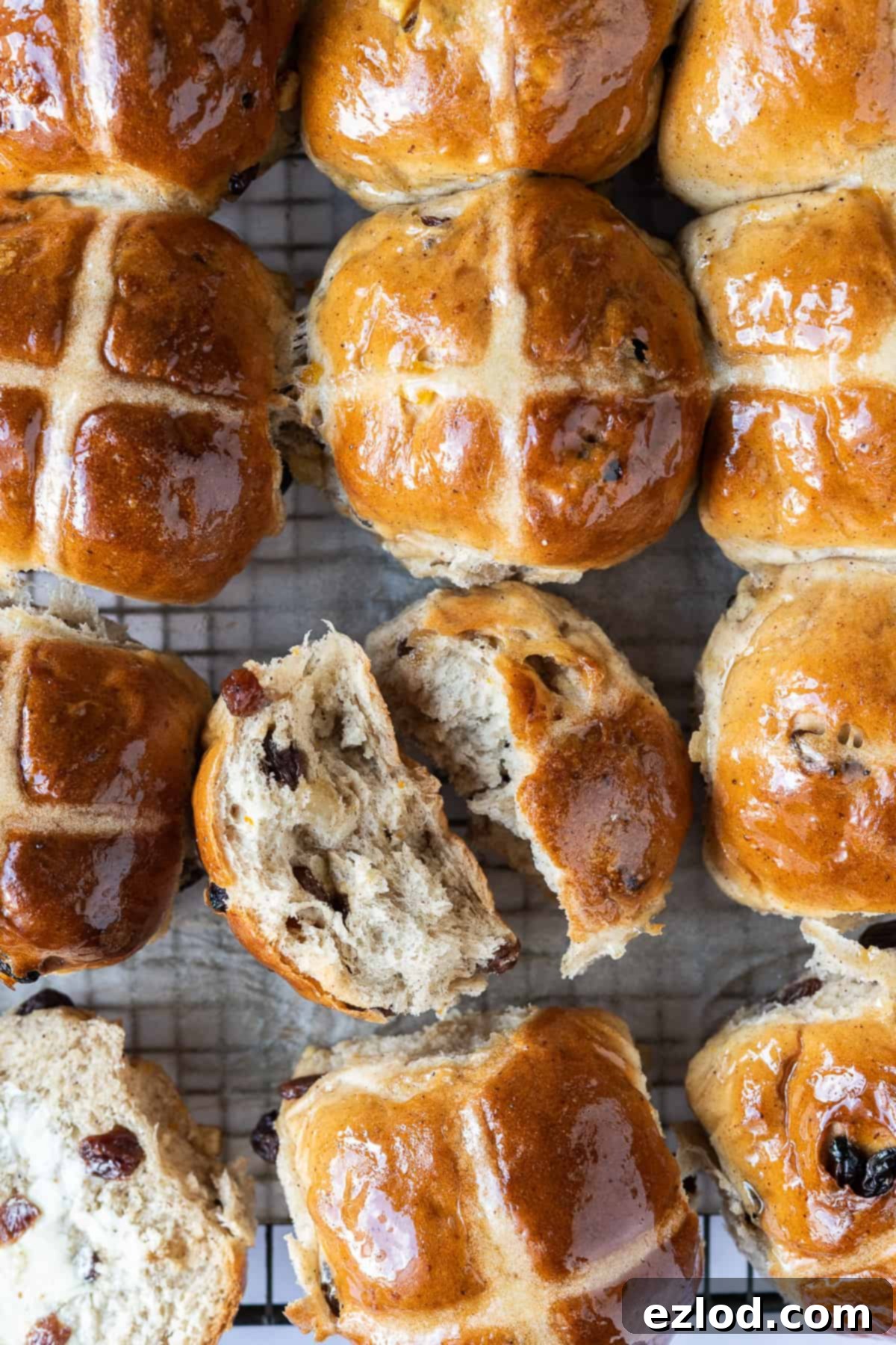 Freshly Baked Vegan Hot Cross Buns - Soft, Spiced, and Ready to Enjoy. #veganbaking #easter #easterrecipes #veganbread #veganrolls Top down shot of several vegan hot cross buns, one torn in half to reveal its fluffy interior and fruit distribution. Emphasizing the soft texture of these dairy-free Easter treats.
