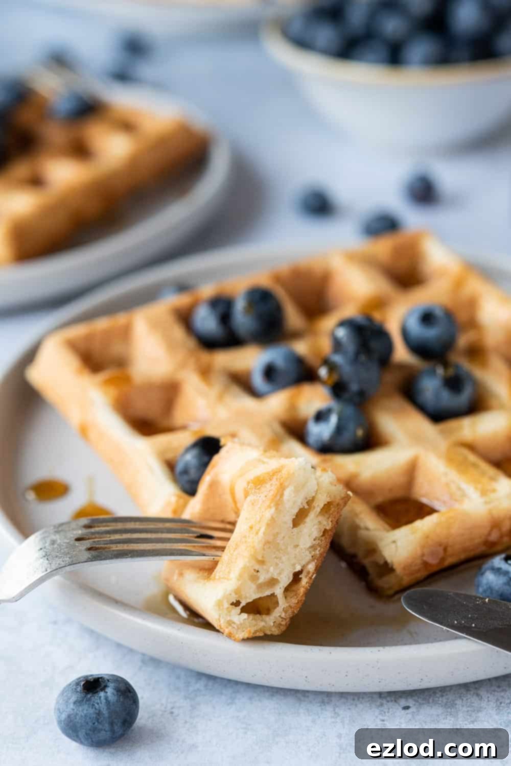 Vegan waffles - these amazing vegan waffles are crispy on the outside and soft and fluffy on the inside; the ultimate vegan breakast! Eggless and dairy free and no banana! Includes options for making them with or without aquafaba. #veganbreakfast #veganwaffles #brunch #breakfast Close up image of a fork taking a bite from a fluffy vegan aquafaba waffle, highlighting its airy and tender texture.