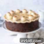Plant-Powered Simnel 6 vegan simnel cake on a white cake stand on a light grey background with a cream cloth, white milk jug and teacups.