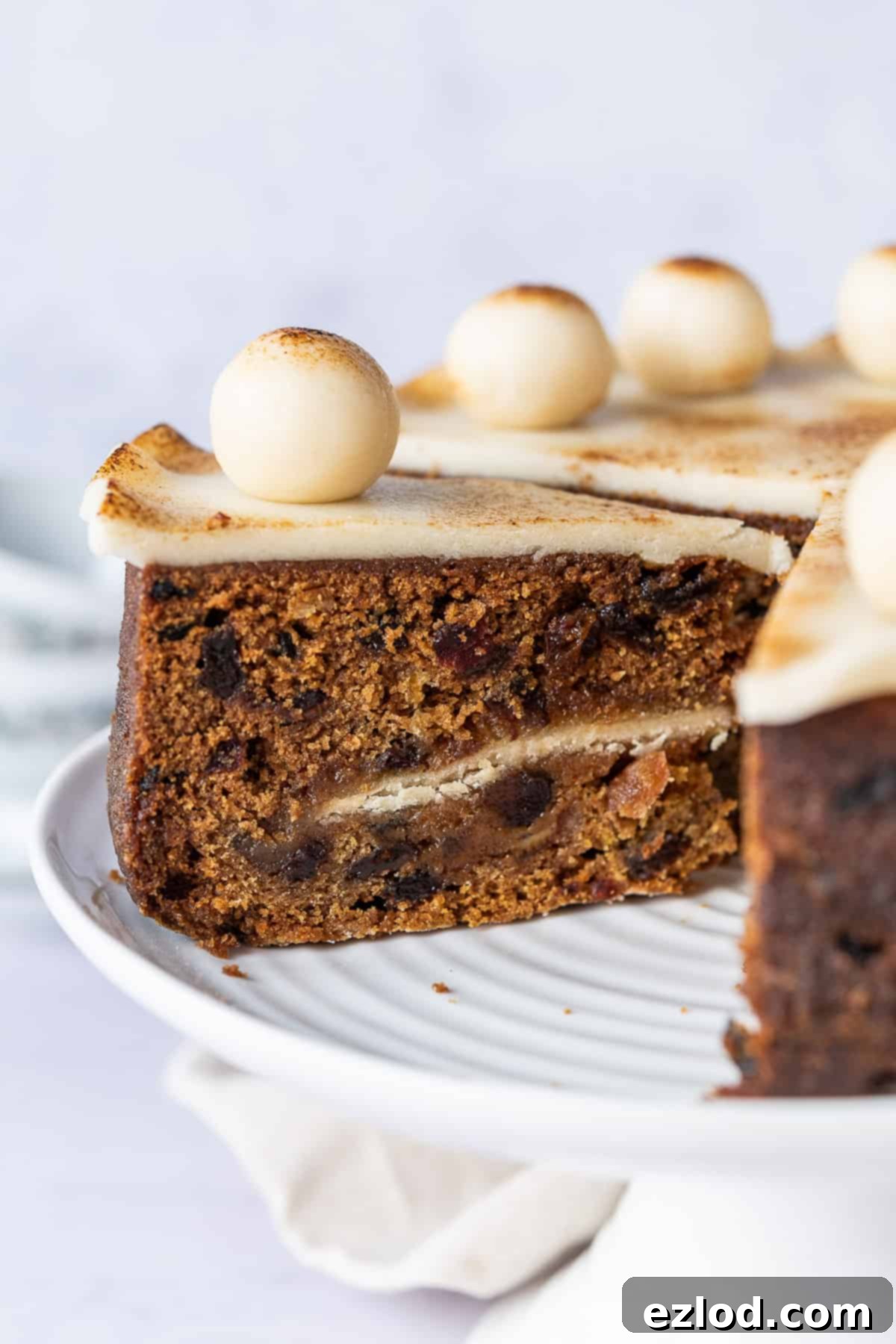 Sliced Vegan Simnel Cake Showing Inner Marzipan Layer A close-up shot of a perfectly sliced vegan Simnel cake, revealing its moist, fruit-studded interior and the inviting layer of marzipan nestled in the middle, highlighting the cake's texture and rich ingredients.