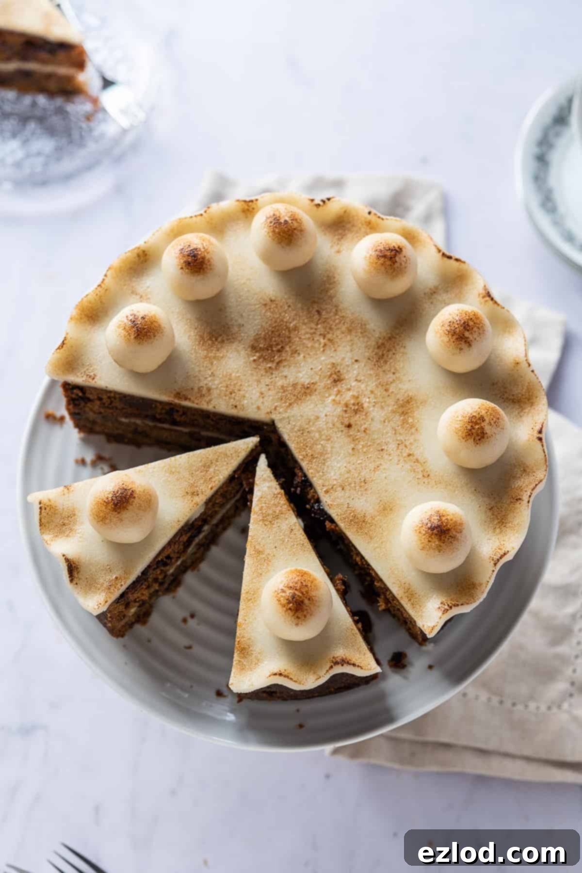 Top View of Sliced Vegan Simnel Cake with Marzipan Balls A top-down view of a vegan Simnel cake on a white cake stand, showcasing the marzipan decorations with several slices already removed, highlighting the cake's delicious cross-section and its festive appeal.