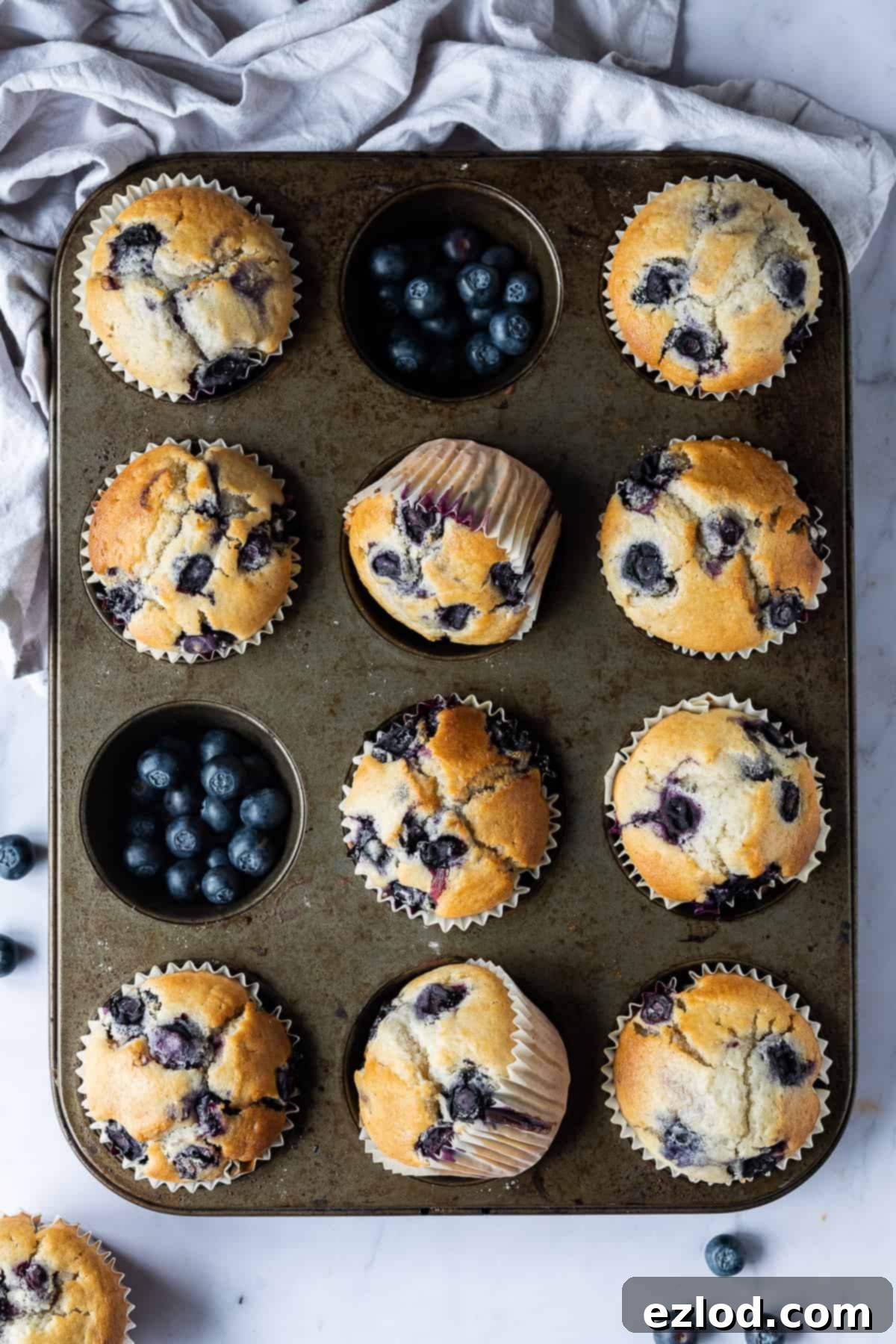 Vegan blueberry muffins - these easy eggless and dairy-free muffins are perfectly light, soft, tender and fluffy with a sweet vanilla flavour and plenty of juicy blueberries. The perfect snack! #veganbaking #veganmuffins #blueberrymuffins #vegansnack #eggless #dairyfree A freshly baked tray of vegan blueberry muffins on a marble background with a grey cloth.