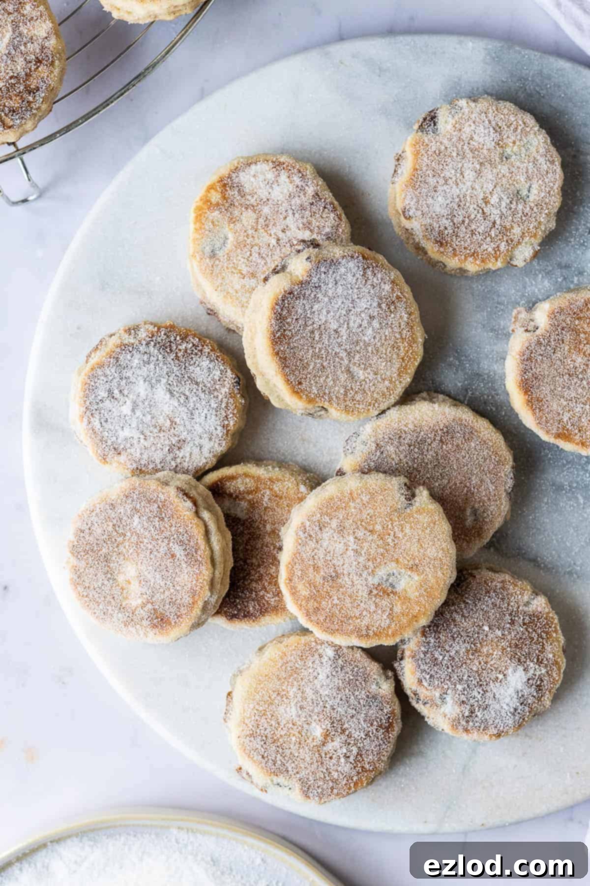 Deliciously Spiced Vegan Welsh Cakes Close up of a pile of sugar-dusted vegan Welsh cakes on a marble board, showcasing their texture.