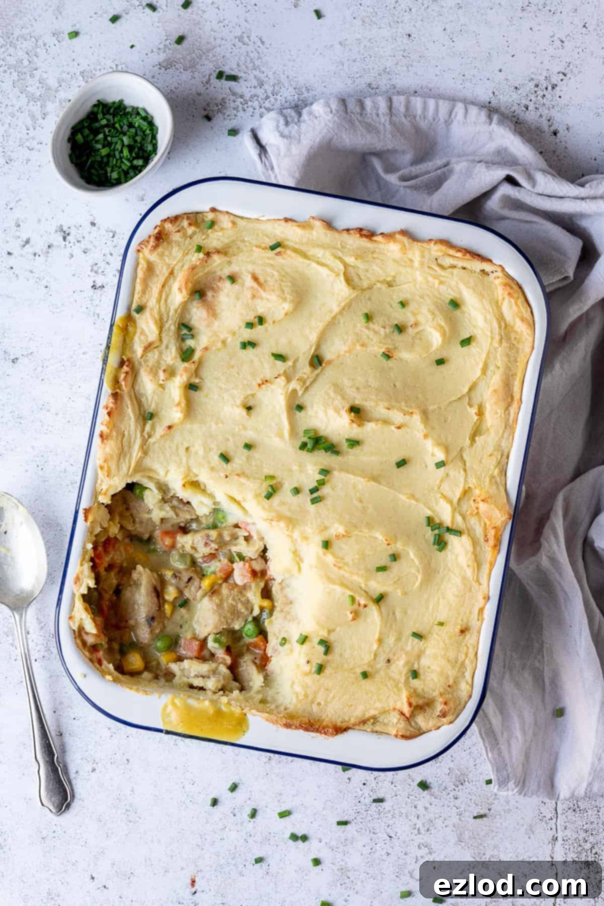 Ultimate Vegan Chicken Potato Pie: A hearty, plant-based comfort food classic with chicken-style soy protein, creamy sauce, and fluffy mashed potato topping. #veganmeal #meatfree #vegandinner #comfortfood A beautifully baked vegan chicken potato pie in an enamel dish, garnished with fresh chives, ready to be served. The golden-brown mashed potato topping is crisp around the edges.