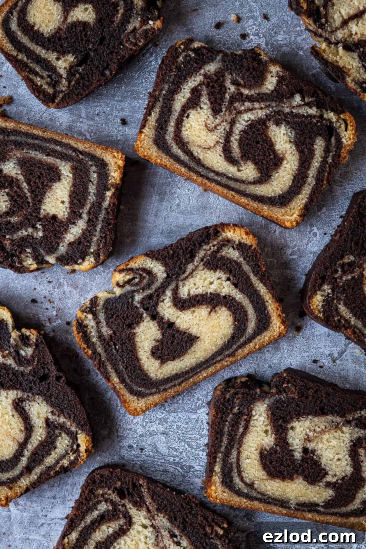 Vegan marble cake - this vegan chocolate and vanilla pound cake is moist, soft and very moreish! It makes a great snack or indulgent breakfast and just look at those swirls! Eggless and dairy-free. #vegancake #veganbaking #loafcake #eggless Slices of the vegan marble cake artfully arranged on a subtle grey background, highlighting the distinct chocolate and vanilla swirls.