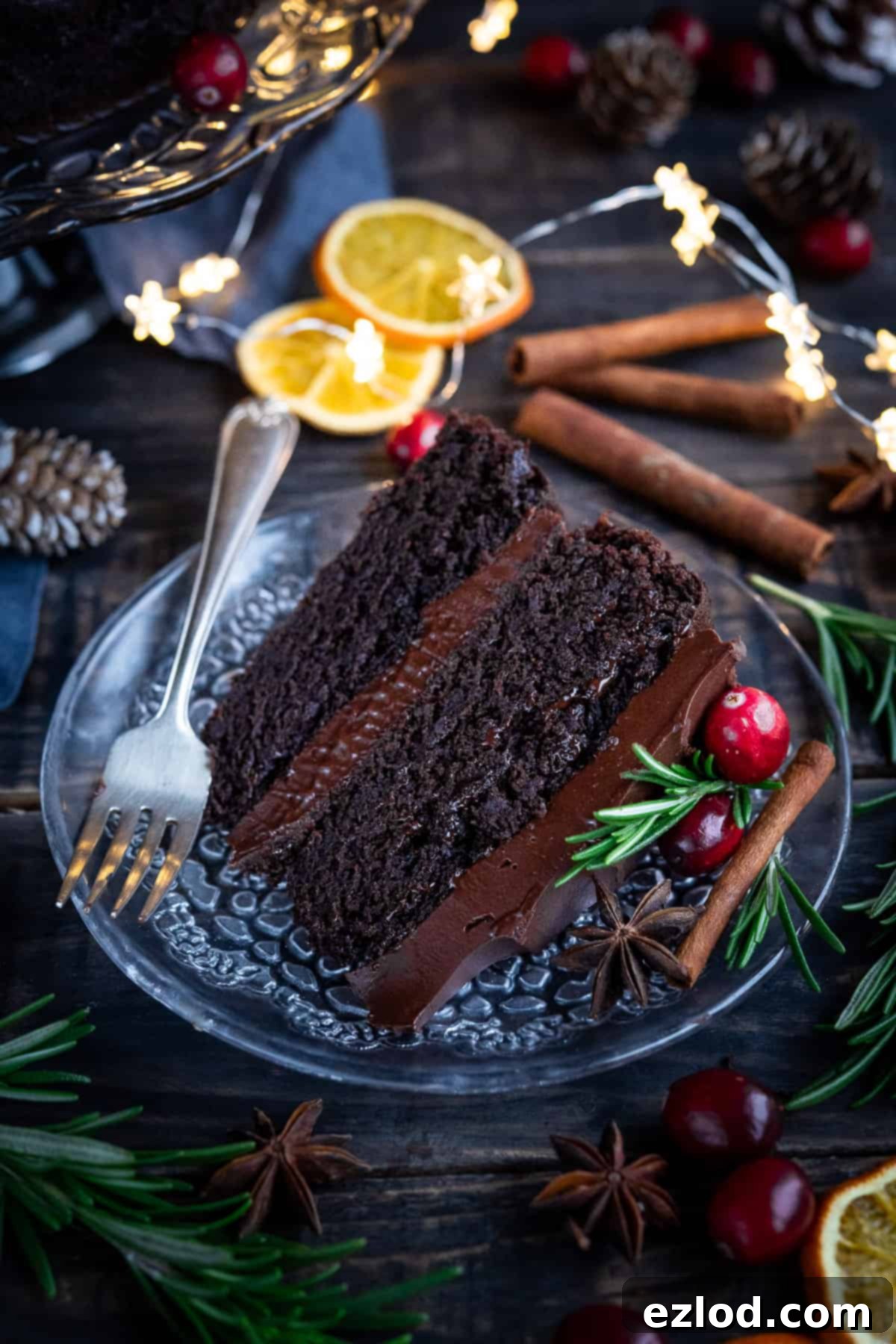 Vegan Mulled Wine Chocolate Cake Slice A slice of chocolate cake on a glass plate with a fork, surrounded by festive decorations.