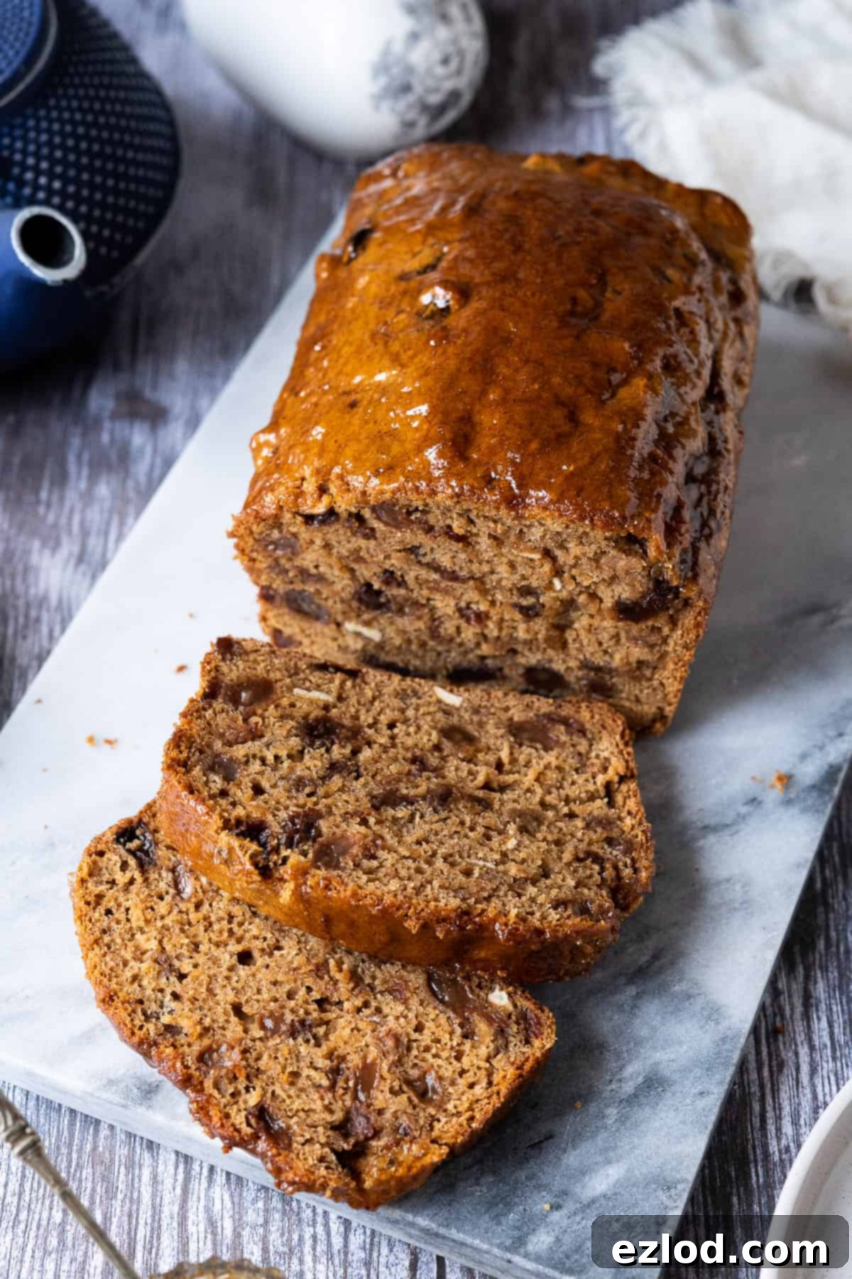 A whole Vegan Earl Grey Tea Loaf – a delicious, easy, fat-free, fruity, eggless, and dairy-free British cake. #veganbaking #vegancake #eggless #loafcake Vegan Earl Grey tea loaf, un-sliced and perfectly baked, sitting on a marble board.