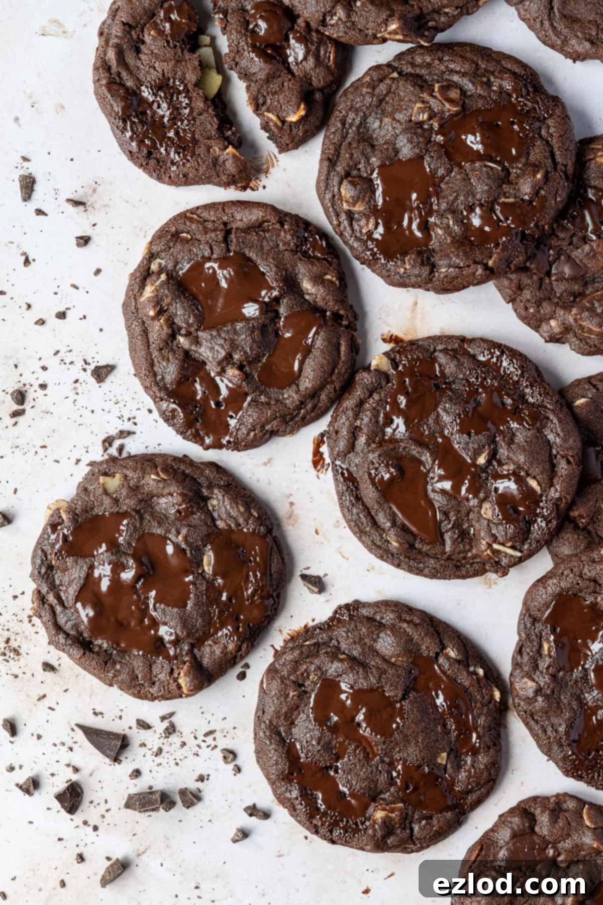 Vegan double chocolate almond almond cookies – these rich, intensely chocolatey cookies are easy to make and taste amazing! They are crisp around the edges, gooey in the middle and are filled with chocolate chunks and almonds for an indulgent treat. Vegan double chocolate almond cookies on a marble surface with a scattering of chopped chocolate.