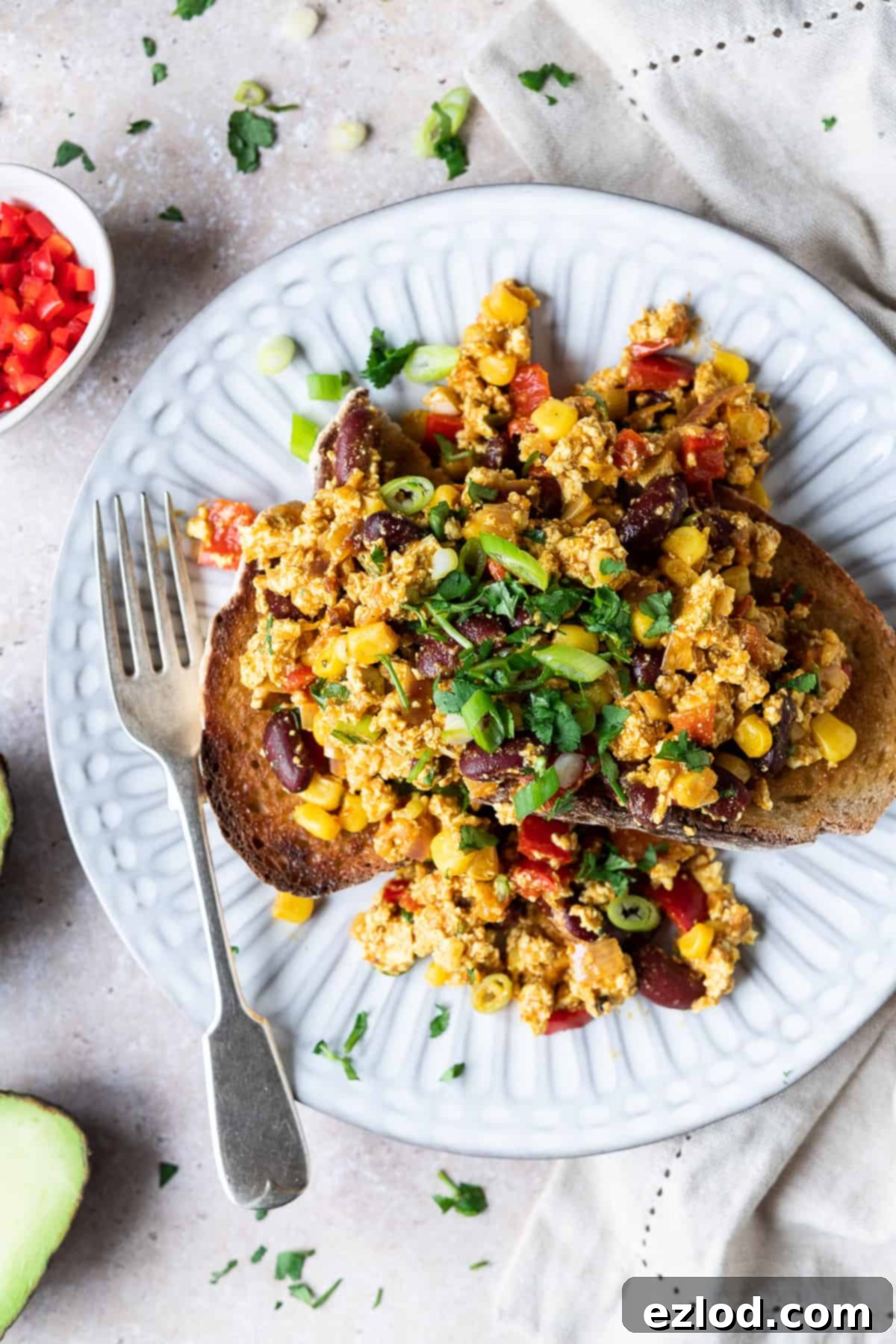Serving Mexican Style Tofu Scramble on Toast - A Healthy, Flavorful, and Protein-Rich Vegan Meal Option #veganbreakfast #veganmeal #plantbased A close-up shot of a single serving of Mexican style tofu scramble piled high on a slice of golden-brown toasted bread, presented on a clean white plate. The scramble is visibly rich with colorful vegetables, suggesting a satisfying and hearty meal. This inviting image showcases a delicious and easy way to enjoy a vegan breakfast, lunch, or dinner.