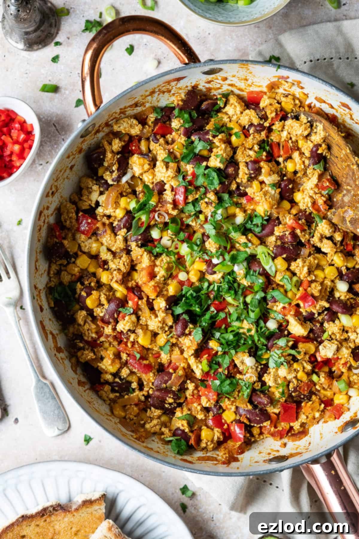 Freshly Cooked Mexican Style Tofu Scramble with Spring Onions and Coriander in Pan - Easy Vegan Recipe #veganmeal #plantbased A vibrant close-up of Mexican style tofu scramble nestled in a white frying pan. The scramble is richly textured and colorful, speckled with finely chopped green spring onions and fresh coriander, ready to be served. This appetizing image highlights the fresh ingredients and appealing presentation of the healthy vegan meal.