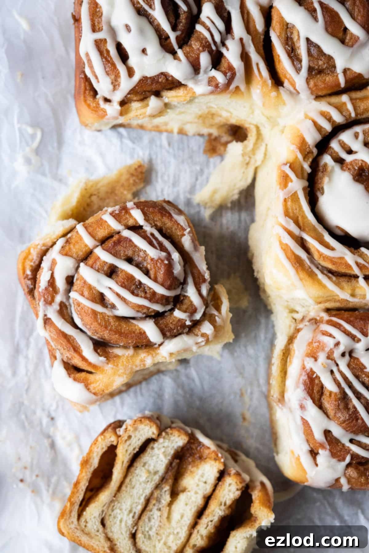Vegan cinnamon rolls - these delicious cinnamon rolls are made using the tangzhong method which makes them incredibly soft, fluffy, squishy and moreish. Eggless and dairy-free. #veganbread #veganbaking #eggless #dairyfree Cinnamon rolls arranged on white baking parchment, with one roll sliced in half to show its soft interior and swirled filling.