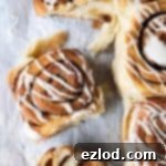 Fluffy Vegan Tangzhong Cinnamon Rolls 6 Cinnamon rolls on white baking parchment, one sliced in half.