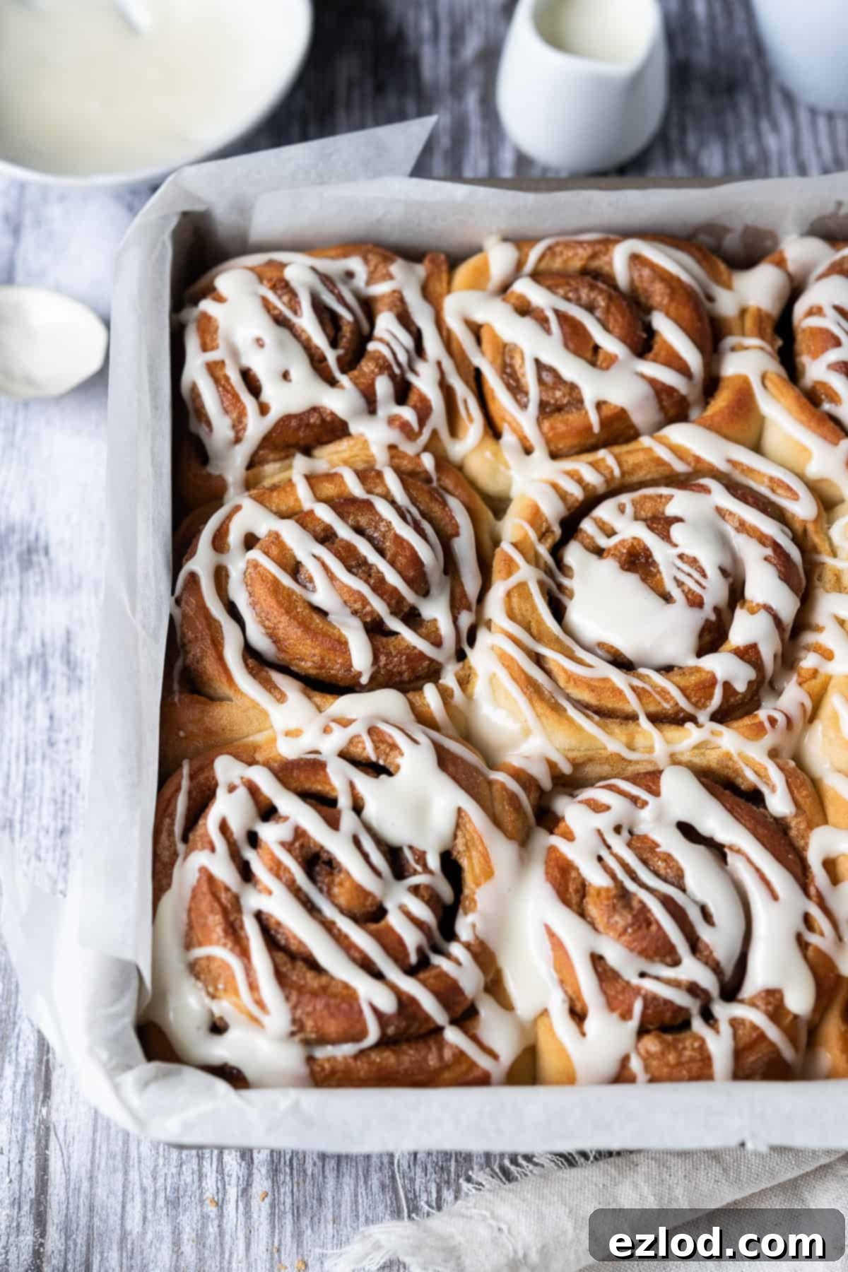 Vegan cinnamon rolls - these delicious cinnamon rolls are made using the tangzhong method which makes them incredibly soft, fluffy, squishy and moreish. Eggless and dairy-free. #veganbread #veganbaking #eggless #dairyfree Close up of perfectly baked cinnamon rolls in a metal cake tin on a wooden table, ready to be glazed.