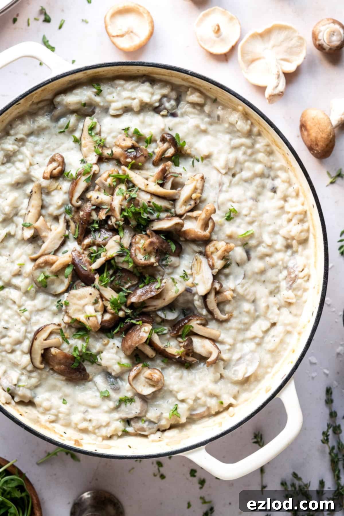 Vegan mushroom risotto with truffle oil – this creamy vegan risotto is full of flavour thanks to earthy mushrooms and truffle oil. Topped with garlic butter shiitake mushrooms it is truly a meal to impress! #veganmeal #plantbased #dairyfree Close-up shot of steaming vegan mushroom risotto in a rustic white cast iron pan, highlighting its rich, creamy texture and visible mushroom pieces.