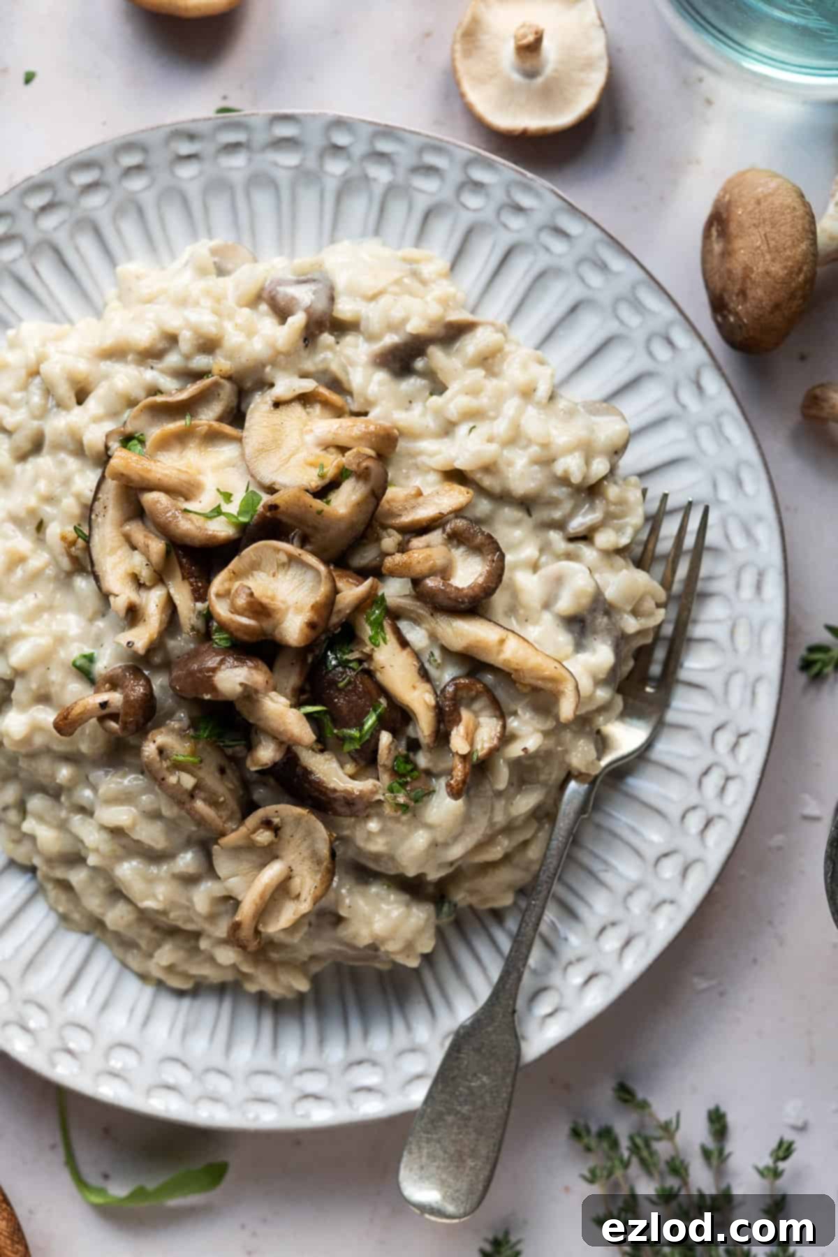 Vegan mushroom risotto with truffle oil – this creamy vegan risotto is full of flavour thanks to earthy mushrooms and truffle oil. Topped with garlic butter shiitake mushrooms it is truly a meal to impress! #veganmeal #plantbased #dairyfree Close-up of a beautifully plated vegan mushroom risotto, garnished generously with golden-brown garlic shiitake mushrooms and fresh green herbs.