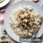 Decadent Vegan Truffle Mushroom Risotto 4 Vegan mushroom risotto topped with fried shiitake mushrooms on a white plate with a bowl of rocket, some fresh mushrooms and thyme.