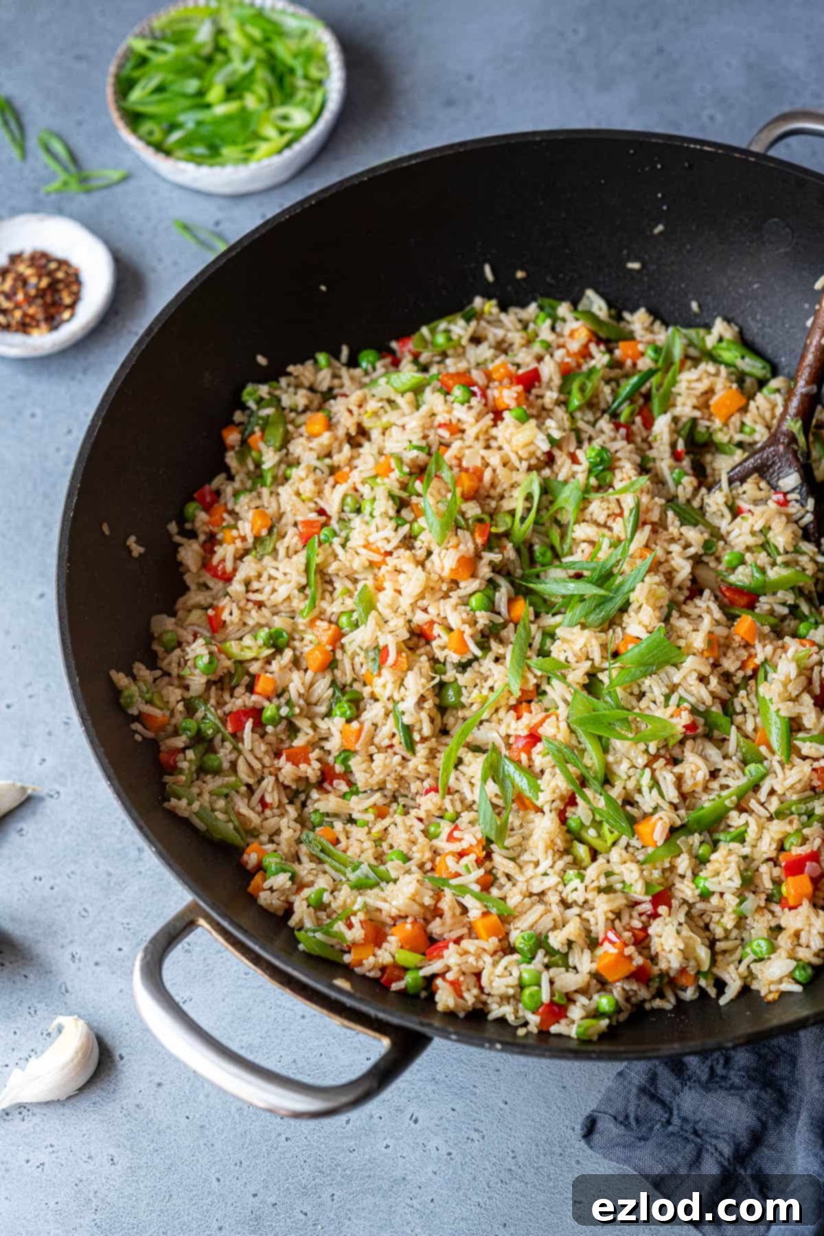 Sizzling vegetable fried rice in a wok, ready to be seasoned. Vegetable fried rice cooking in a wok, with ingredients like spring onions and chili flakes in small bowls nearby.