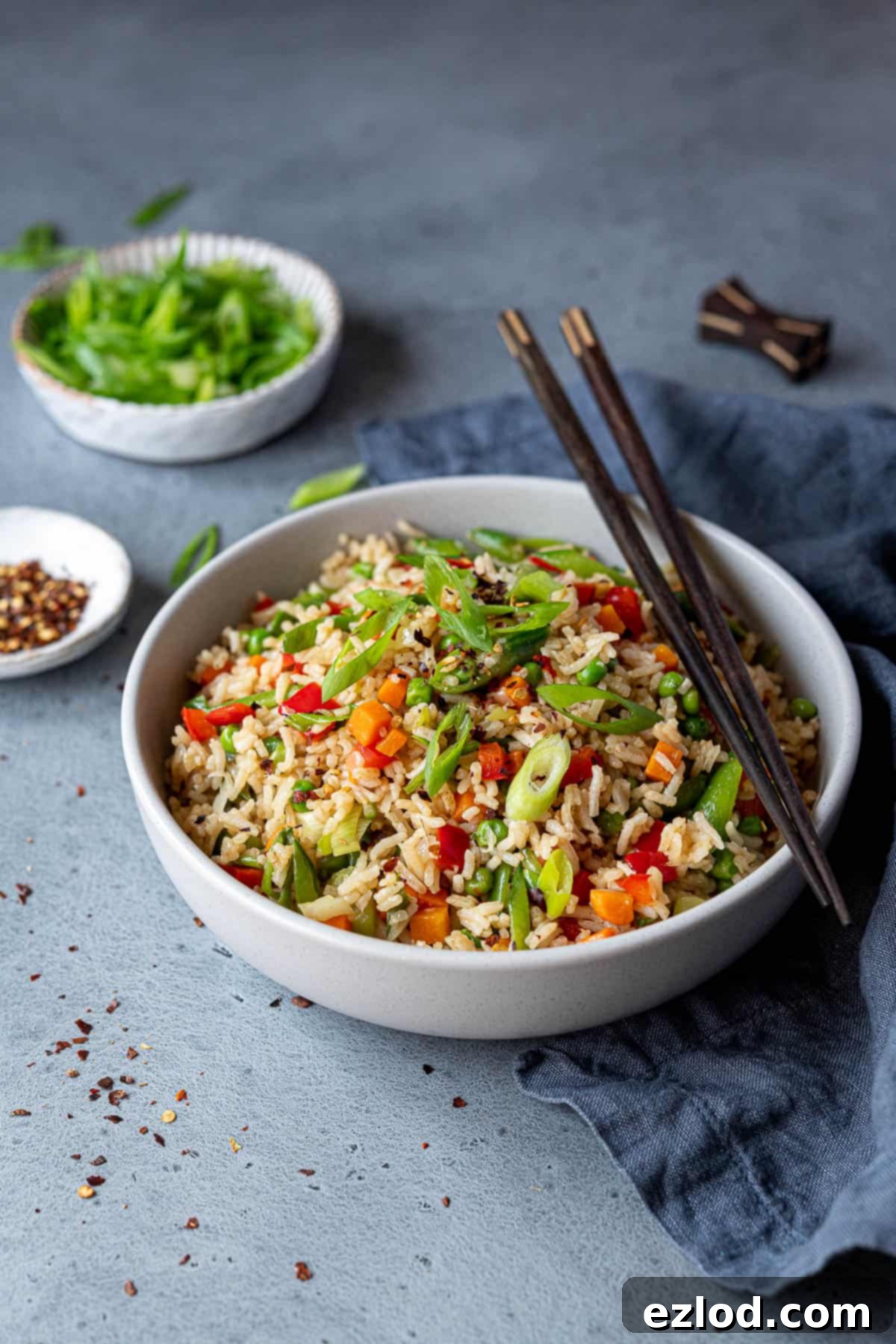 Delicious vegan vegetable fried rice served with chopsticks. A bowl of freshly made vegetable fried rice, garnished with spring onions and chili flakes, with chopsticks ready for serving.