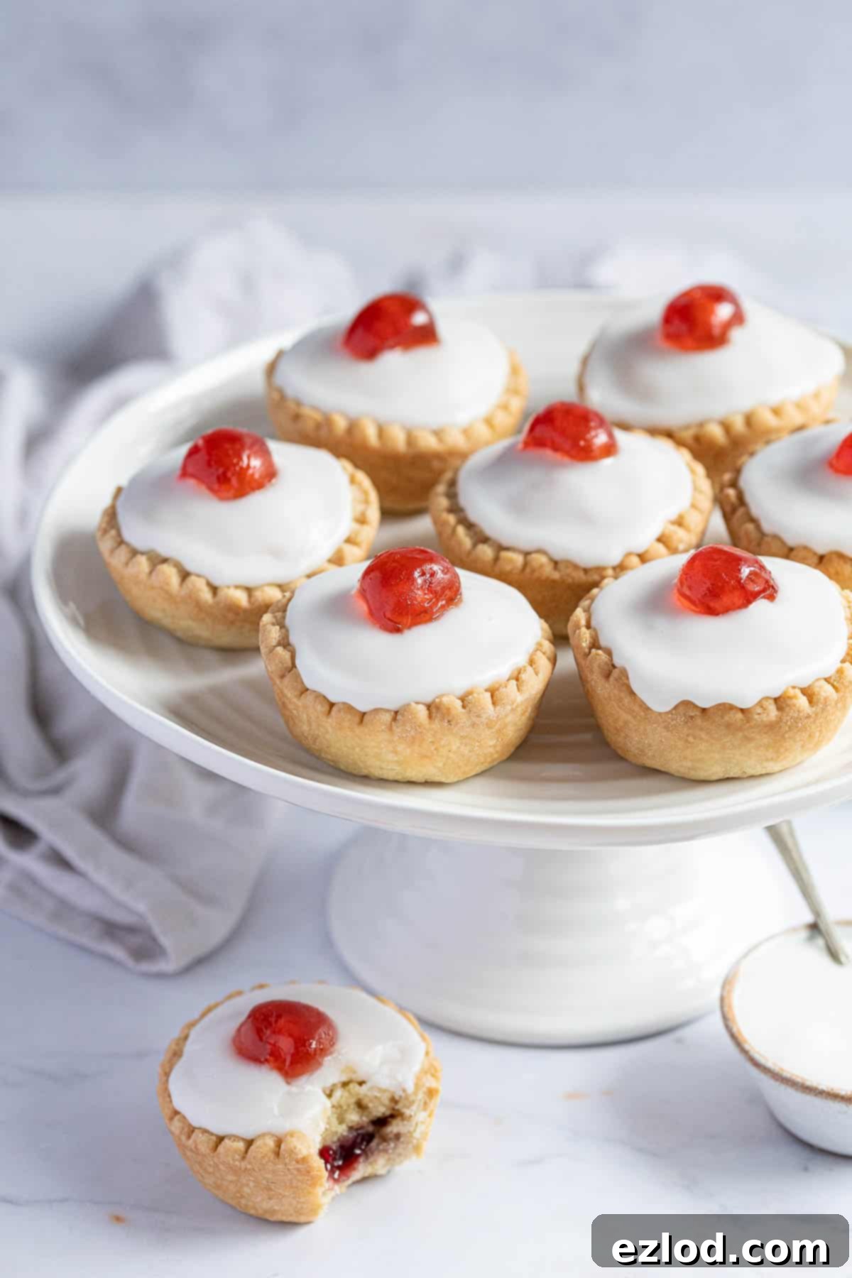 Irresistible Vegan Cherry Bakewells 12 Vegan cherry Bakewells on a white cake stand.