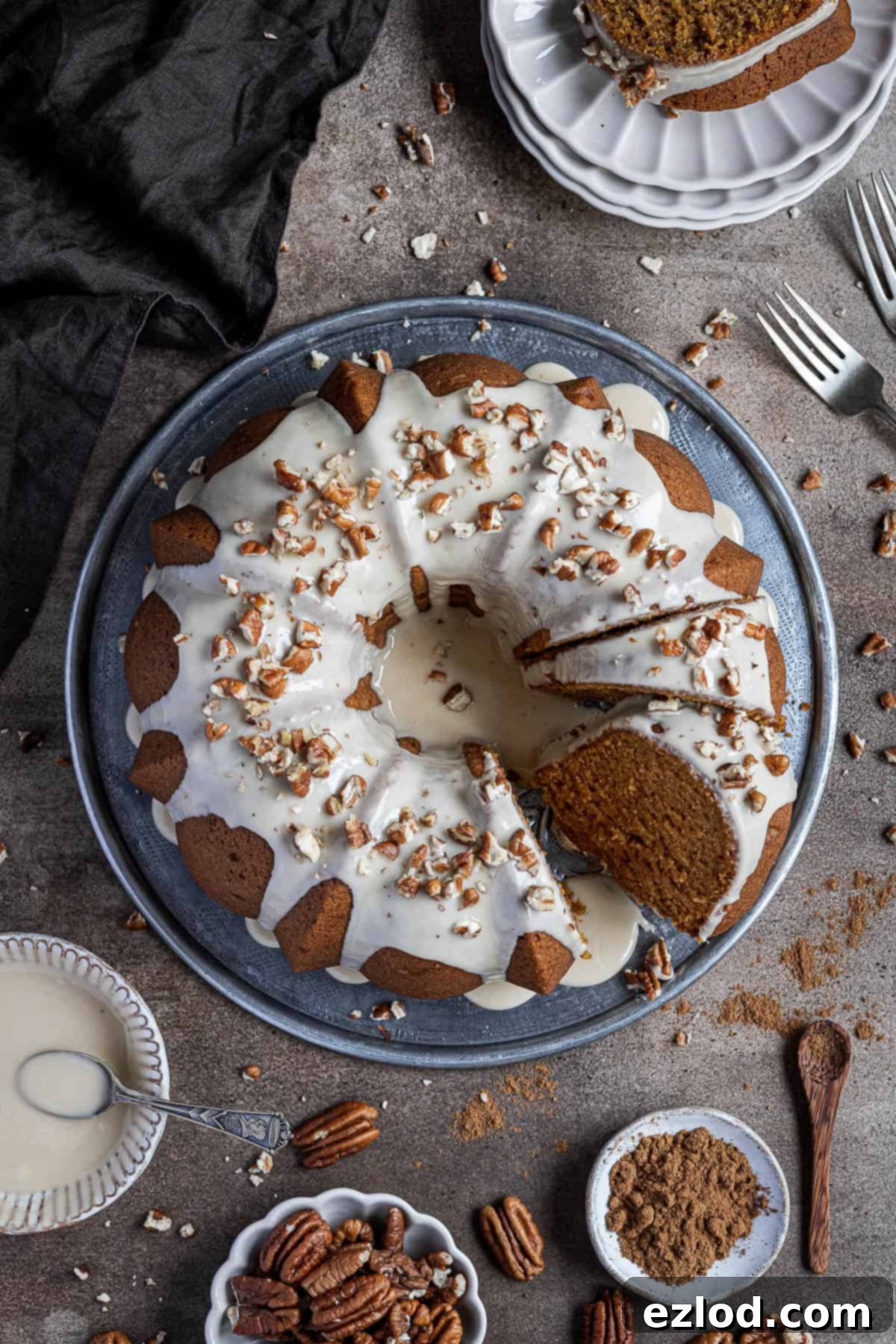 Cozy Vegan Pumpkin Bundt Delight 2 A beautifully crafted vegan pumpkin bundt cake displayed on a rustic metal plate, accompanied by small bowls of maple glaze, crunchy pecans, and aromatic pumpkin spice blend. The cake is moist and ready to be served.