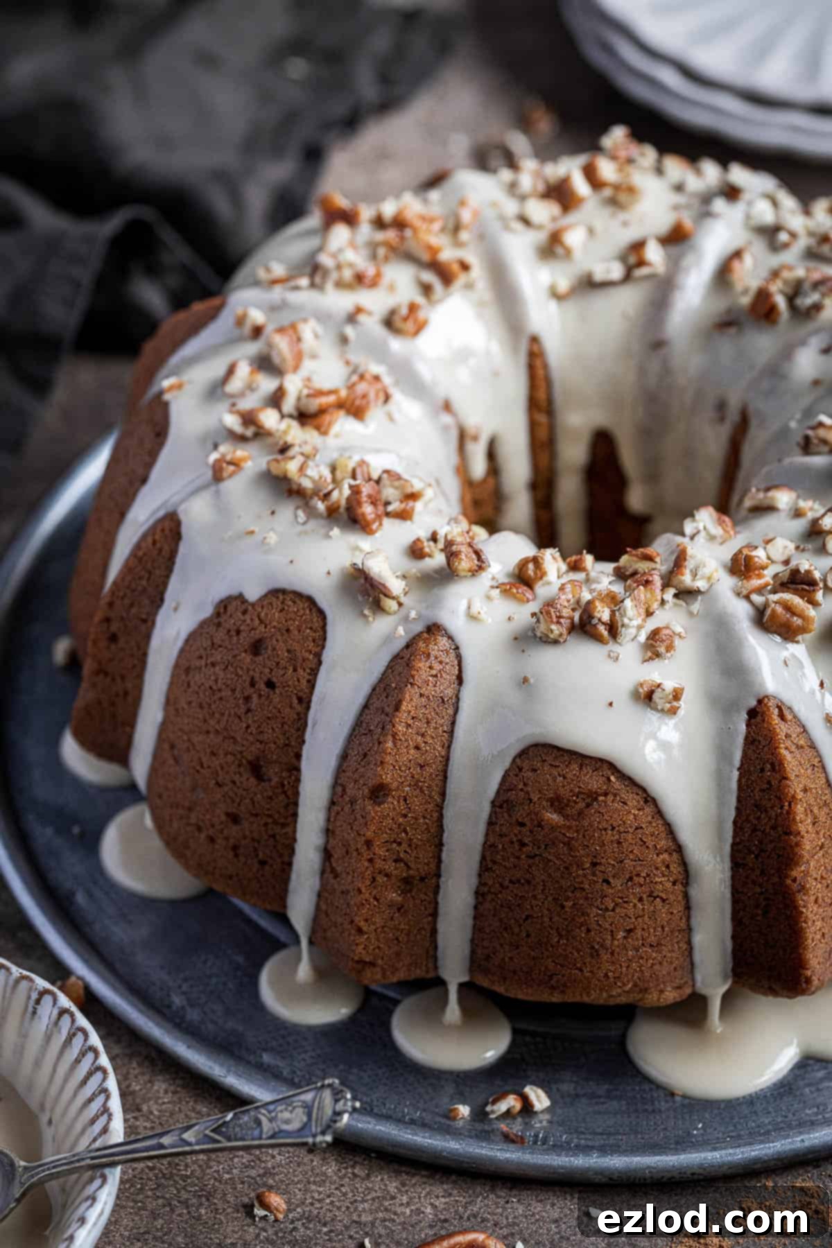 Cozy Vegan Pumpkin Bundt Delight 3 A close-up view of the golden-brown vegan pumpkin bundt cake, generously drizzled with a smooth maple glaze and garnished with chopped pecans, highlighting its inviting texture and festive appeal.