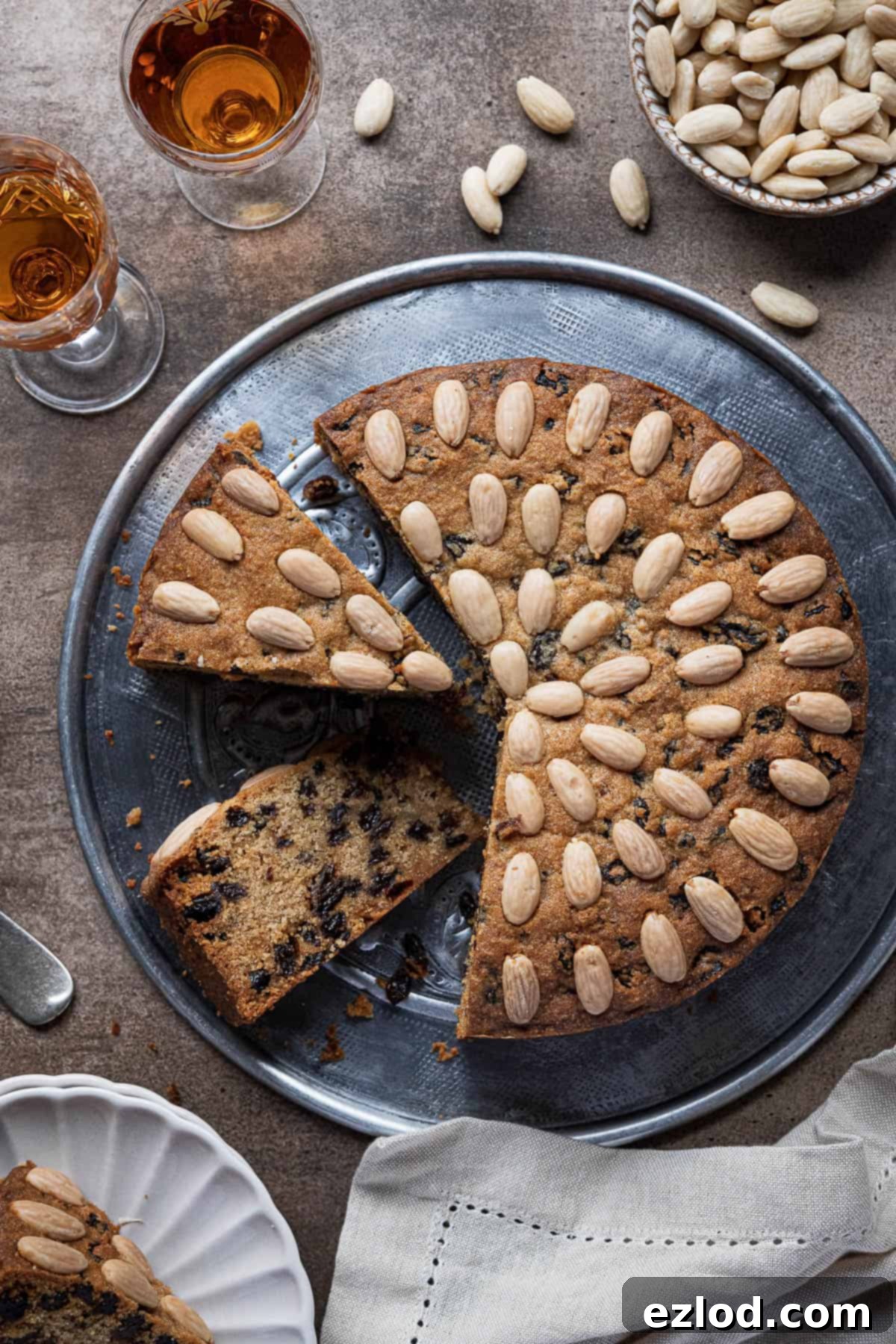 Plant-Based Dundee Cake 2 Vegan Dundee cake with three slices cut on a metal plate with glasses of whisky and a bowl of almonds.