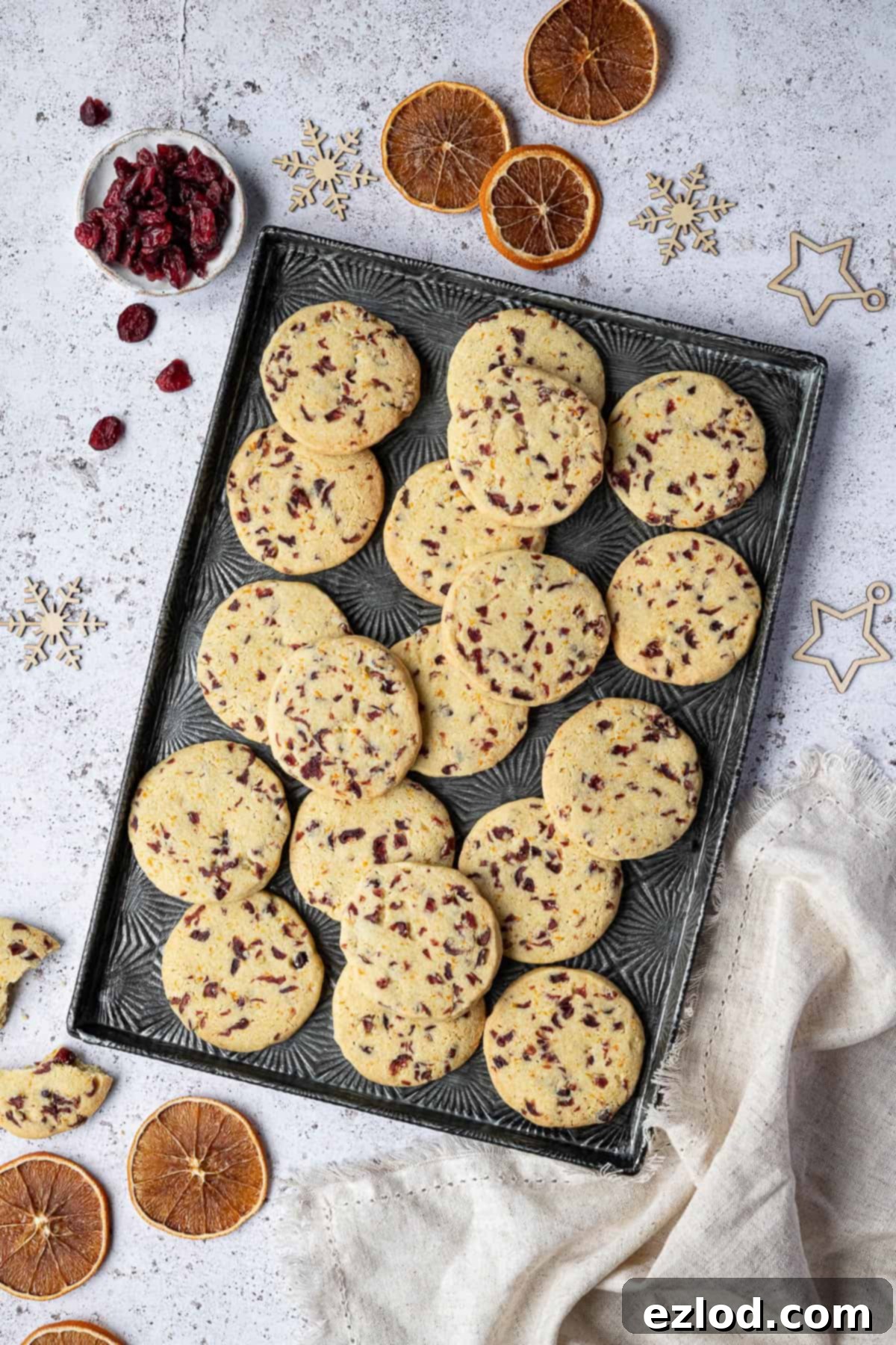 Vegan Zesty Cranberry Orange Shortbread 3 Freshly baked vegan shortbread cookies displayed on a metal tray, adorned with dried orange slices, cranberries, and charming Christmas ornaments, setting a holiday mood.