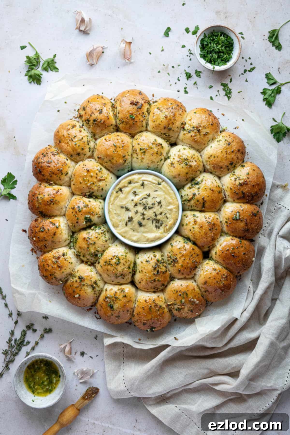 Pillowy Vegan Garlic Dough Balls 2 A beautiful wreath of golden brown vegan garlic dough balls, generously brushed with garlic butter, arranged around a small bowl of creamy cashew cheese dip. Fresh herbs are scattered nearby, highlighting the vibrant flavors.